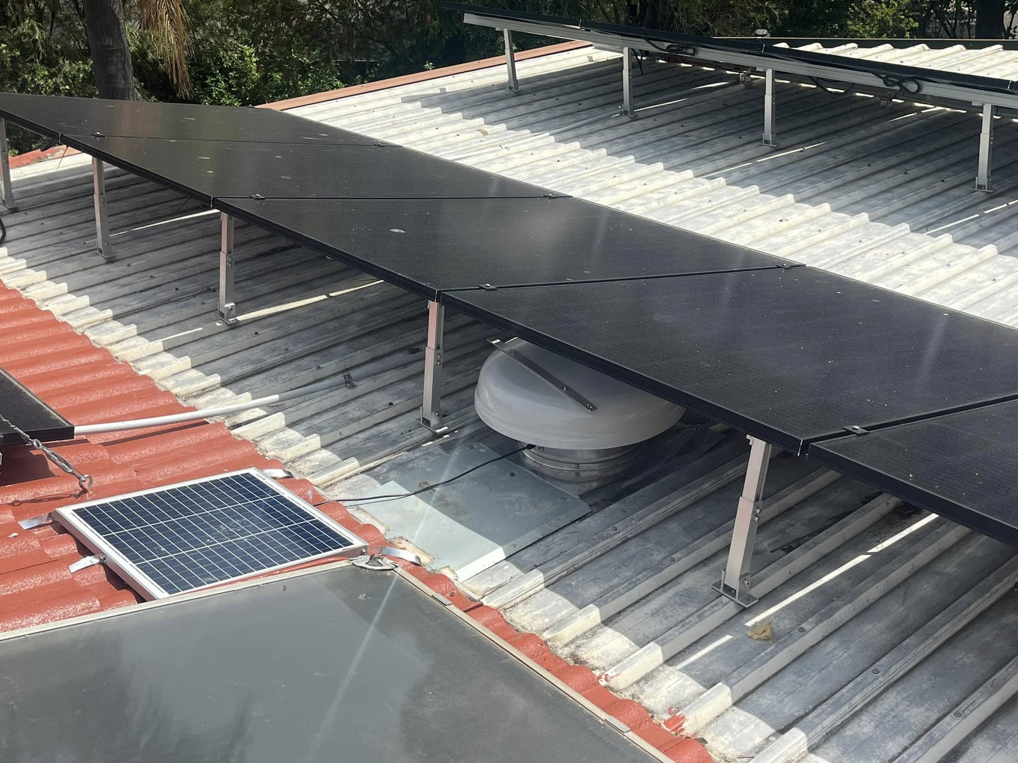 SolarWhiz roof ventilator installed beneath an existing solar panel array on a corrugated roof