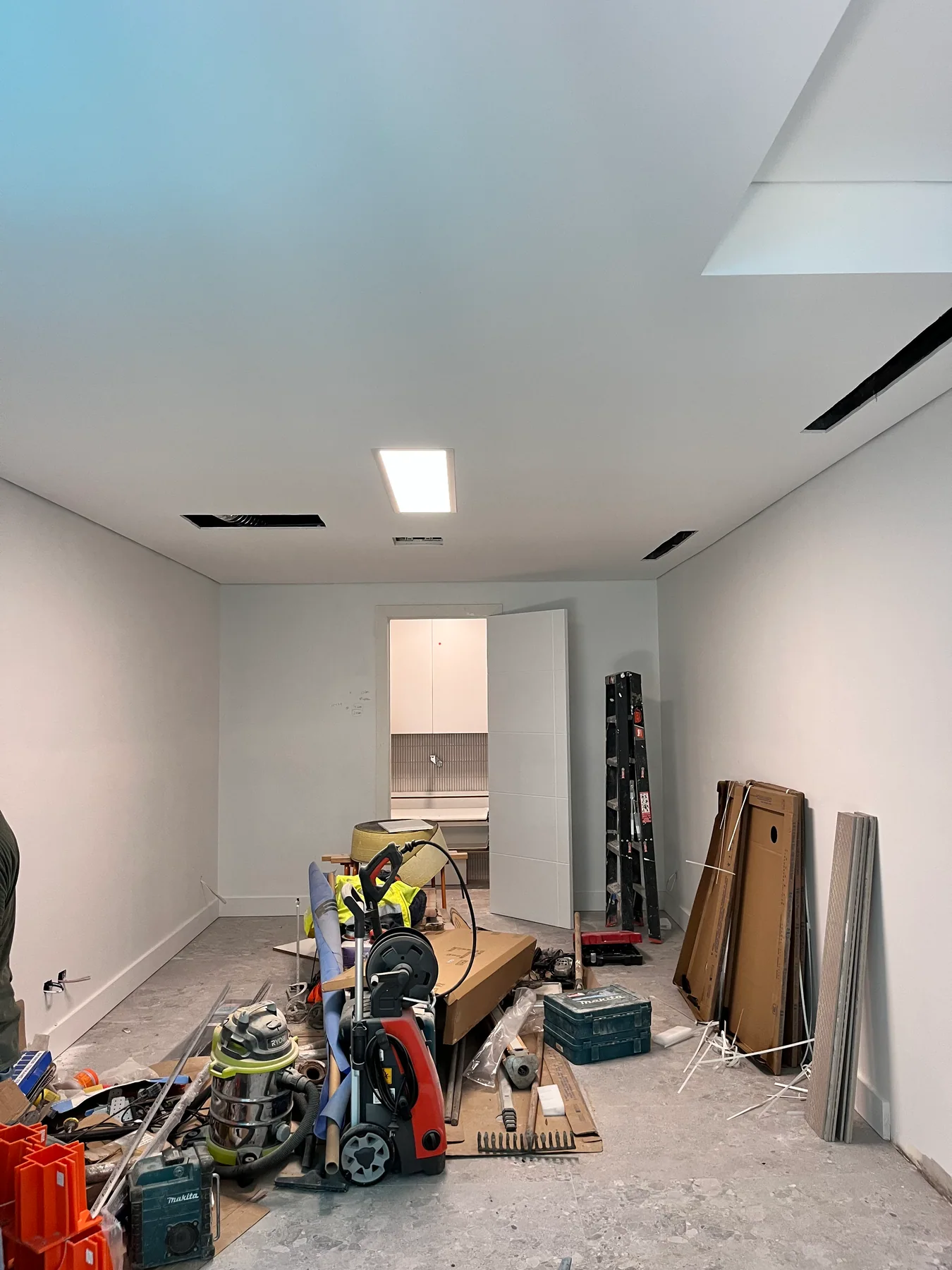 Randwick new-build room during fit-out, with illuminated ceiling panel, open service slots and materials on the floor